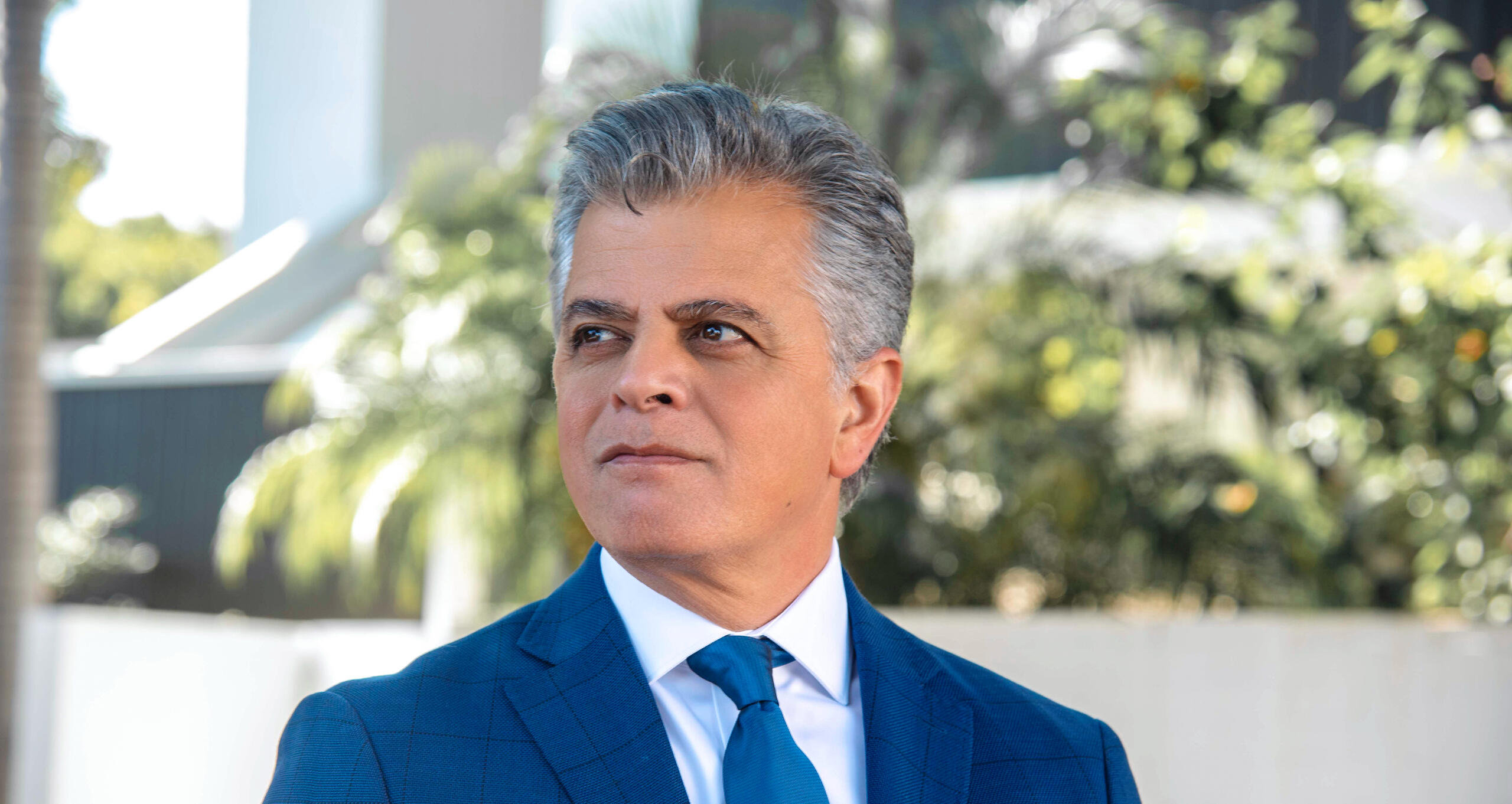 Professional headshot of a distinguished man in a blue suit, gazing off-camera with confidence. Captured outdoors in natural light, conveying leadership, clarity, and executive presence.